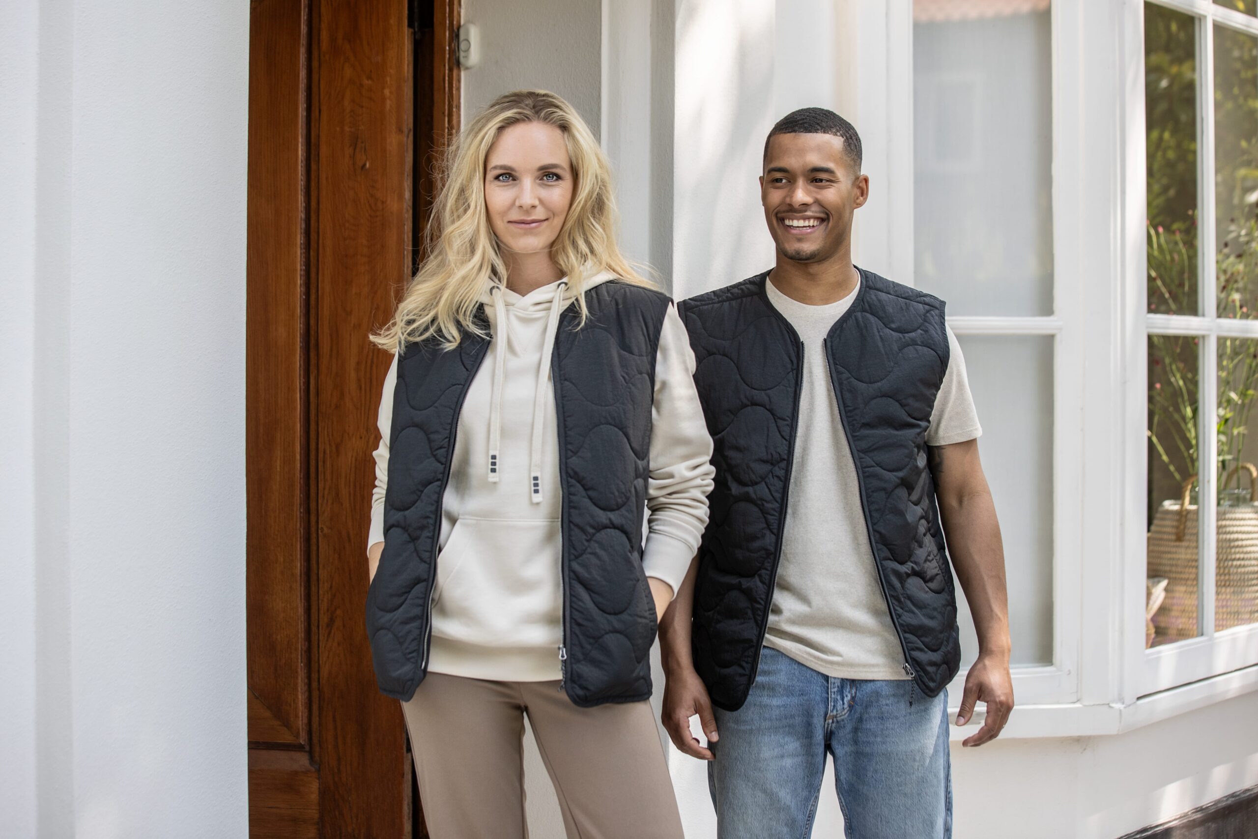 Two people wearing branded clothing standing by a window